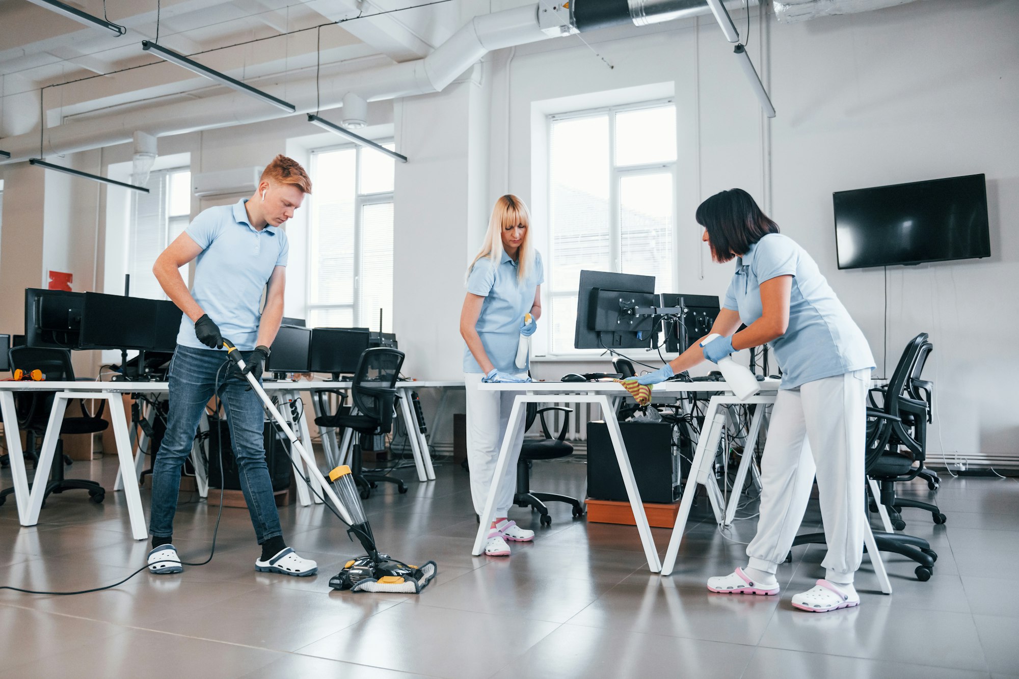 Cleans floor. Group of workers clean modern office together at daytime