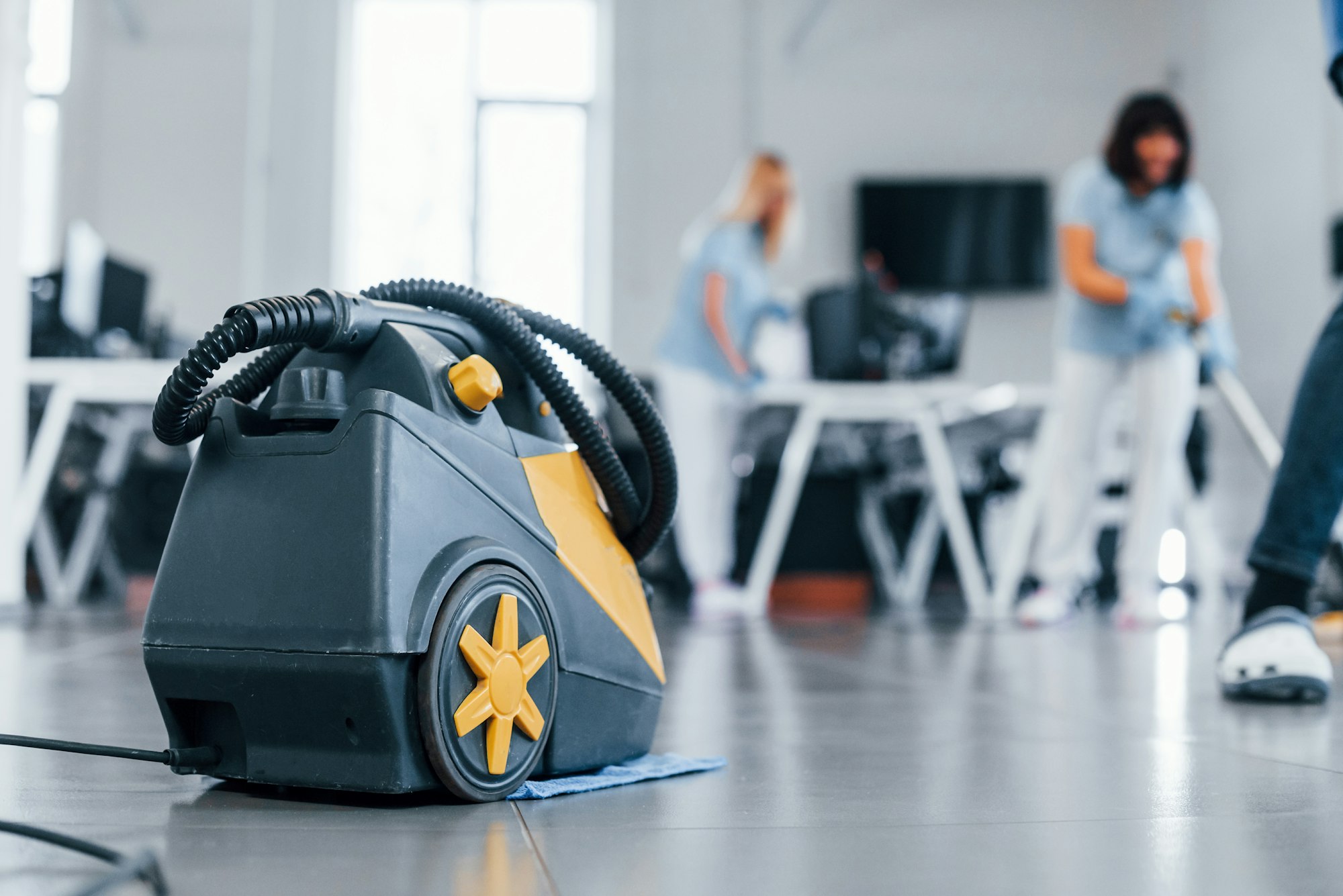 Woman uses vacuum cleaner. Group of workers clean modern office together at daytime